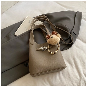 Détail d'un sac seau en cuir grainé marron avec boucle argentée et breloque ourson