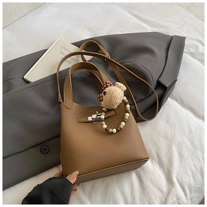 Détail du sac seau en cuir marron avec motif litchi, fermoir argenté et breloque ours