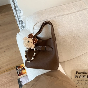 Detail view of coffee leather bucket bag with plush bear charm and beaded handle on sofa