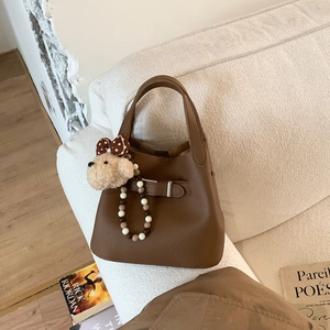 Detail of brown litchi pattern leather bucket bag with cute plush bear charm on a sofa