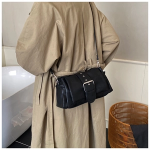 Detail of black leather crossbody bag with wide grommet buckle strap on a trench coat