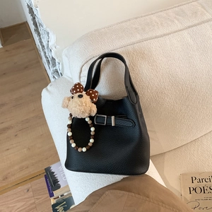 Detail of black lychee leather bucket bag with a cute plush bear and beaded handle