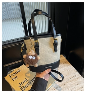 Detail of grey canvas bucket bag with black leather trim and cute brown plush monster charm