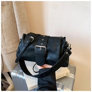 Detail of a black matte leather shoulder bag with wide decorative strap buckle on a suitcase