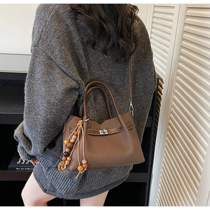 Détail d'un sac à main marron en cuir grainé avec pompon perlé et fermoir pivotant en métal