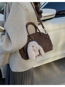 Deep brown matte leather tote bag with plush bunny charm shown in an outdoor street setting
