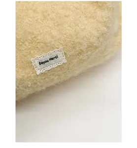 Dettaglio del tessuto in lana di agnello beige con etichetta in pizzo del marchio
