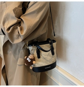 Detail view of stylish beige bucket bag featuring black leather trim and a cute teddy charm