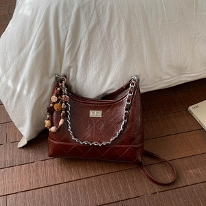 Gros plan du sac en cuir matelassé marron foncé avec fermoir argenté et charms