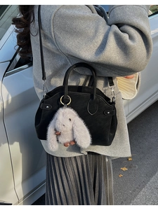 Detail of a black matte leather shell bag with top handles and a cute bunny pendant