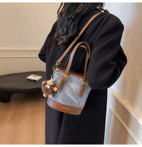 Detail of blue denim bucket bag with brown leather trim and cute monster plush charm