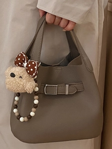 Handheld beige lychee grain bucket bag with cute bear charm and belt buckle detail
