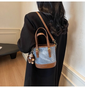Detail of denim bucket bag with brown leather trim and a plush monster charm accessory
