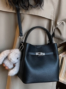Sac seau en cuir litchi noir avec poignée et breloque lapin gris sur fond de trench-coat