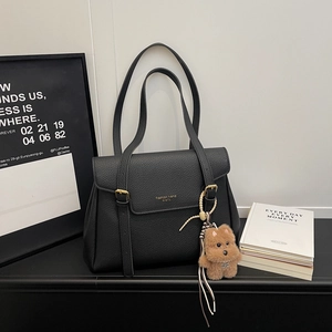 Détail d'un sac cabas en cuir noir avec logo doré et breloque petit chien en peluche doux
