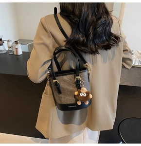 Detail of grey bucket bag with plush charm and fashion text, shown in a lifestyle setting