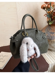Detail of dark green leather tote with plush rabbit charm and detachable shoulder strap