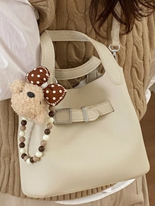 Chic beige bucket bag with metal buckle, bear pendant and beaded strap on knit sweater