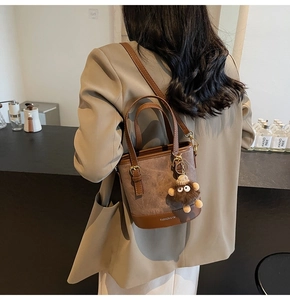 Detail view of retro suede bucket bag with long strap and cute monkey charm on model