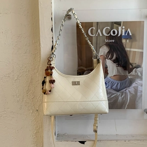 Détail du sac matelassé crème avec fermoir rotatif argenté et breloque décorative élégante