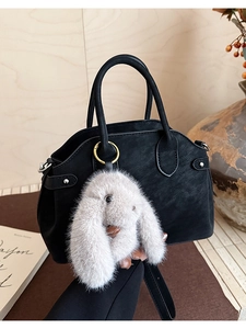 Detail view of a black matte leather shell bag with a fluffy white plush bunny charm