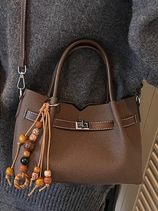 Sac à main minimaliste en cuir marron foncé avec pompon sur un pull gris chiné
