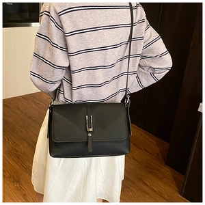 Detail showing the black litchi texture leather crossbody bag on a model shoulder