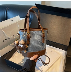 Detail of denim bucket bag with brown leather trim and a cute plush bear charm