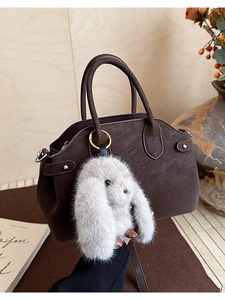 Detail view of dark brown lychee texture handbag with a soft plush bunny charm