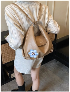 Detail of khaki shoulder bag with blue checkered floral patch and logo in indoor setting