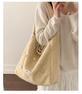 Dettaglio della borsa tote in pile beige con toppe a stella ed etichetta in pizzo su modella