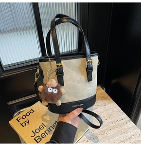 Detail of canvas bucket bag featuring leather base, brand logo and plush charm accessory