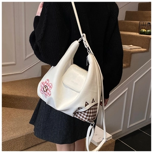 Close-up of white leather shoulder bag with pink floral patches and brown check details