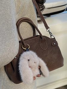 Dark brown minimalist leather handbag with a pink plush bunny charm and silver strap hooks