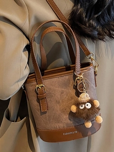 Brown canvas bucket bag with leather trim and plush charm shown on model