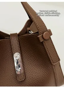 Detail van de bruine handtas van lychee-leer met zilveren metalen slot en fijne stiksels