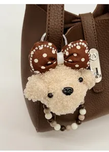 Detail van een schattige pluche hondenhanger aan een bruine leren bucket bag