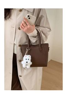 Detail of dark brown leather bucket bag with a white plush puppy charm on the handle