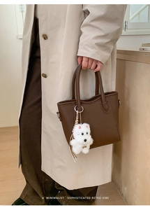 Detail of retro brown lychee leather bucket bag with cute plush puppy charm accessory