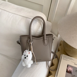 Detail of taupe litchi grain leather bucket bag with cute white plush puppy charm pendant