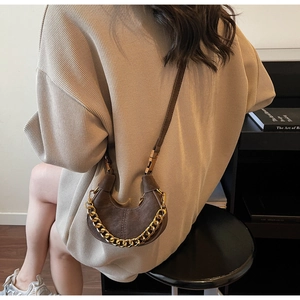 Détail d'un sac demi-lune marron foncé avec chaîne dorée sur fond de pull en maille