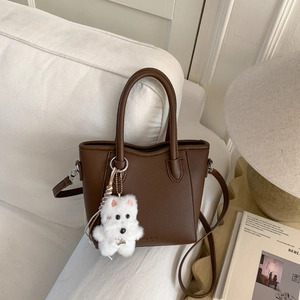 Detailed close-up of brown litchi grain leather bucket bag with cute plush puppy charm