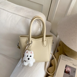 Close-up of cream leather tote bag with lychee texture and cute plush puppy charm