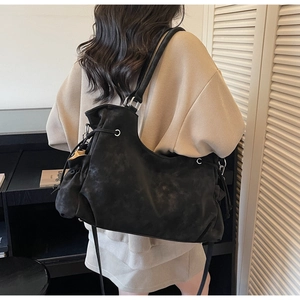 Detail of black suede tote bag with drawstring closure and metallic ring accents