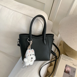 Detail of black lychee grain bucket bag with a plush dog charm on a white sofa
