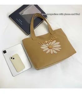 Detail of khaki canvas tote bag with daisy embroidery compared to iPad and phone size