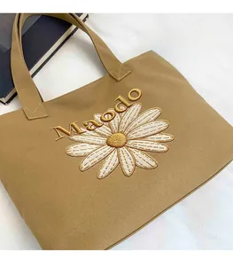 Detailed view of khaki canvas tote bag featuring large daisy floral embroidery and text
