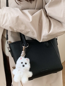 Black pebble leather bucket bag with white plush dog charm and silver metal hardware