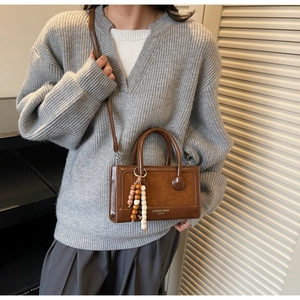 Detail of a brown leather handbag with fashion logo and decorative wooden bead charm