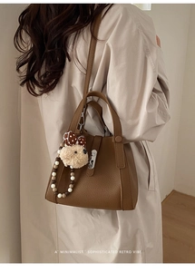 Detail van retro bruine lederen emmer tas met teddybeer bedeltje en gekleurde kralen handvat
